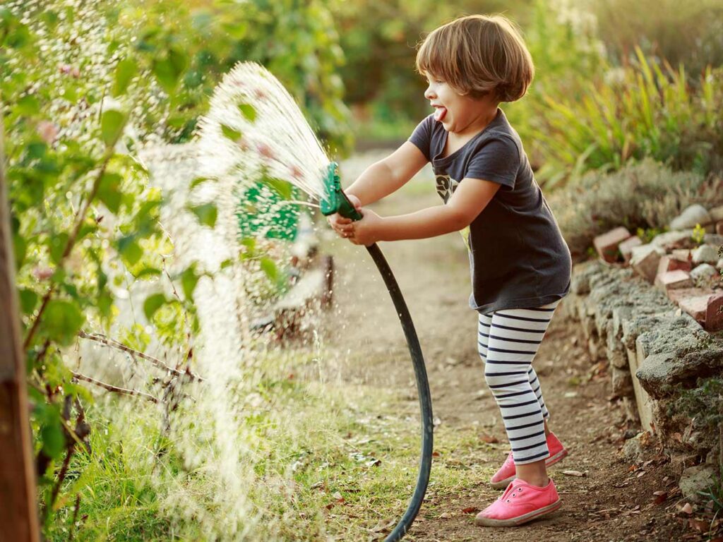 Young girl playing with a water hose in her family's garden