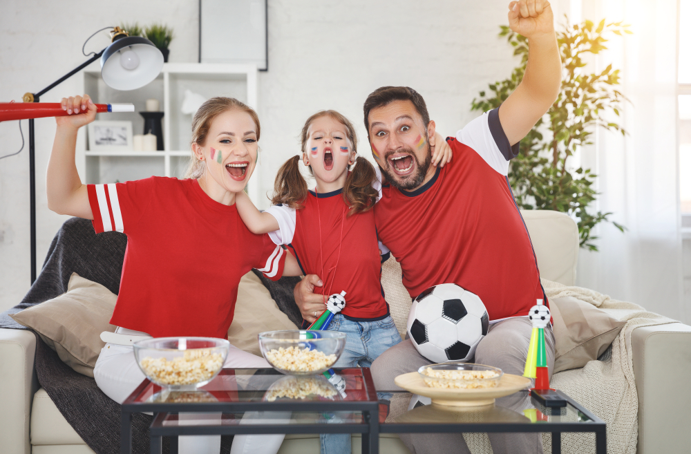 A family of fans in red football kits watching a football match on TV at home