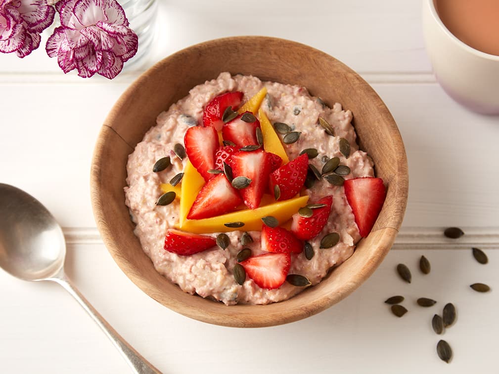 Wooden bowl of gluten-free oats topped with mango, strawberries and chai seeds