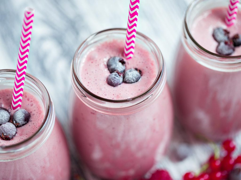 Three glasses of pink berry milkshakes topped with three blueberries each