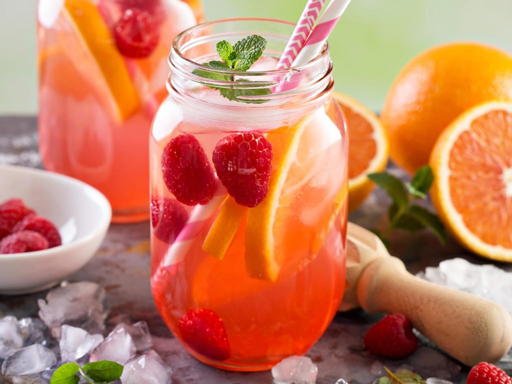 Photograph of two glasses of pink lemonade with orange slices and raspberries