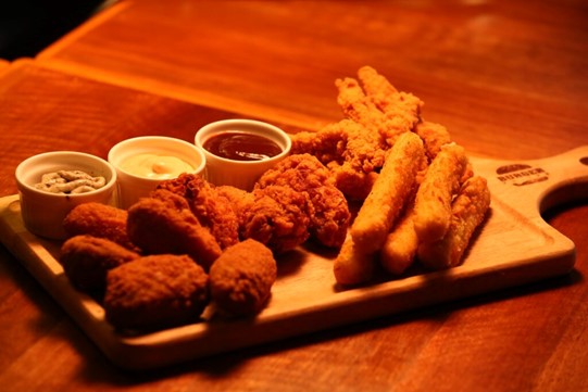 Chicken dippers, mozzarella sticks and different types of dipping sauces on a wooden board