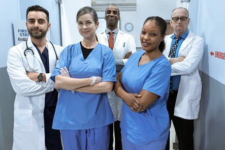 Photograph of two female nurses and three male doctors in scrubs standing upright with their arms crossed