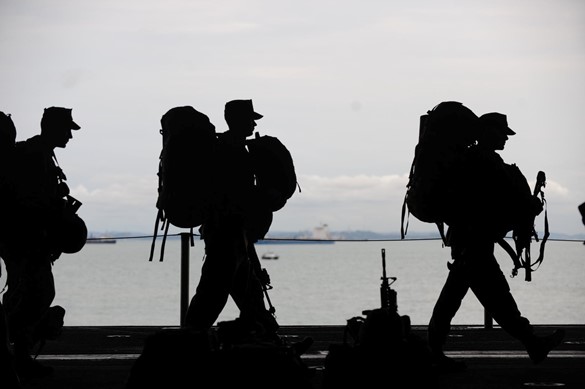 Silhouette of three soldiers with backpacks and guns against an ocean backdrop