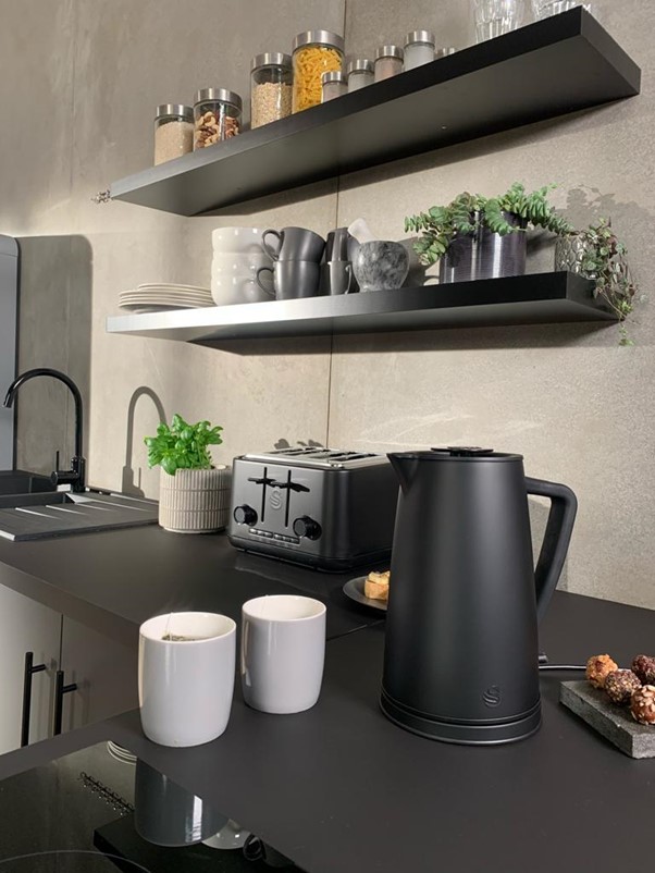 Stealth Matte Black Kettle on a black countertop next to two light grey mugs of tea with the Stealth 4 slice toaster in the background