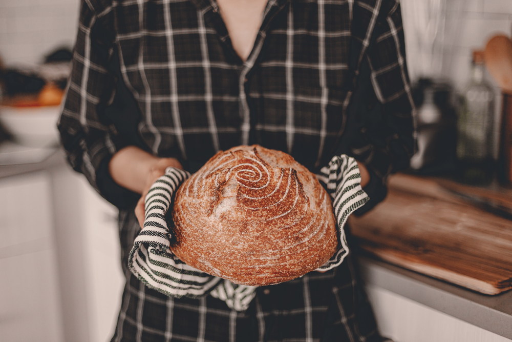Woman holding homemade loaf of sourdough bread in her kitchen