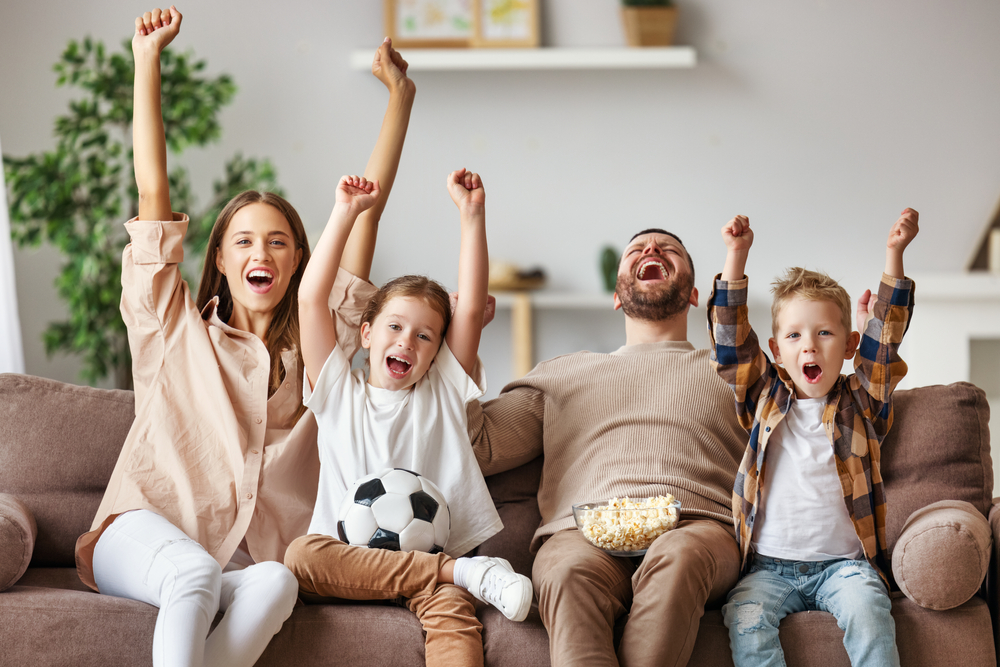 Mother, father and children watching Euros 2020 final in their living room with a bowl of popcorn and football