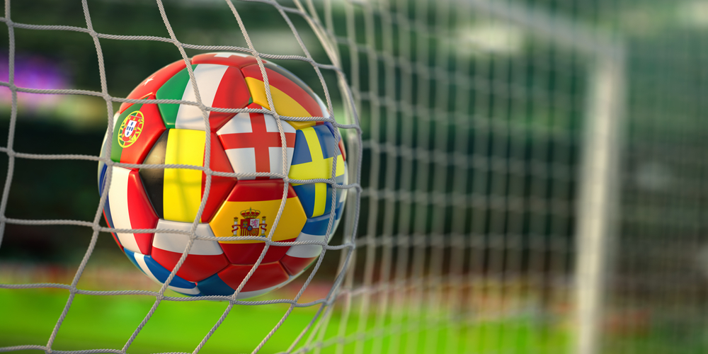 Photograph of a football with different countries' flags printed on it at the back of a white football goal net