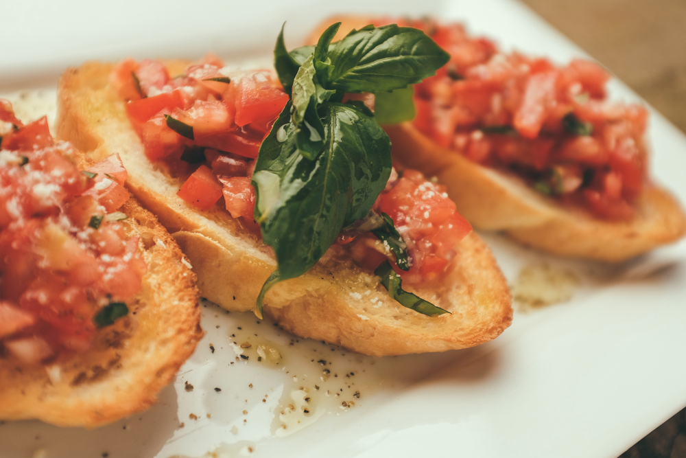 closeup shot of bruschetta with tomato and basil on a white plate