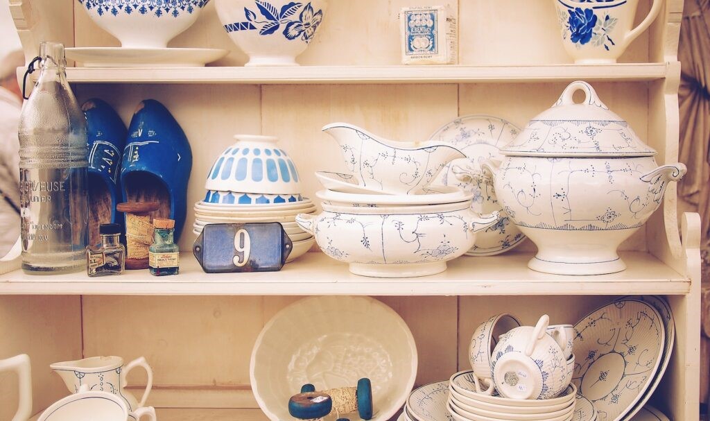 Image of shelves with a range of afternoon tea crockery including bowls, teacups and saucers, plates, jugs, glasses and pots with white and blue patterns.