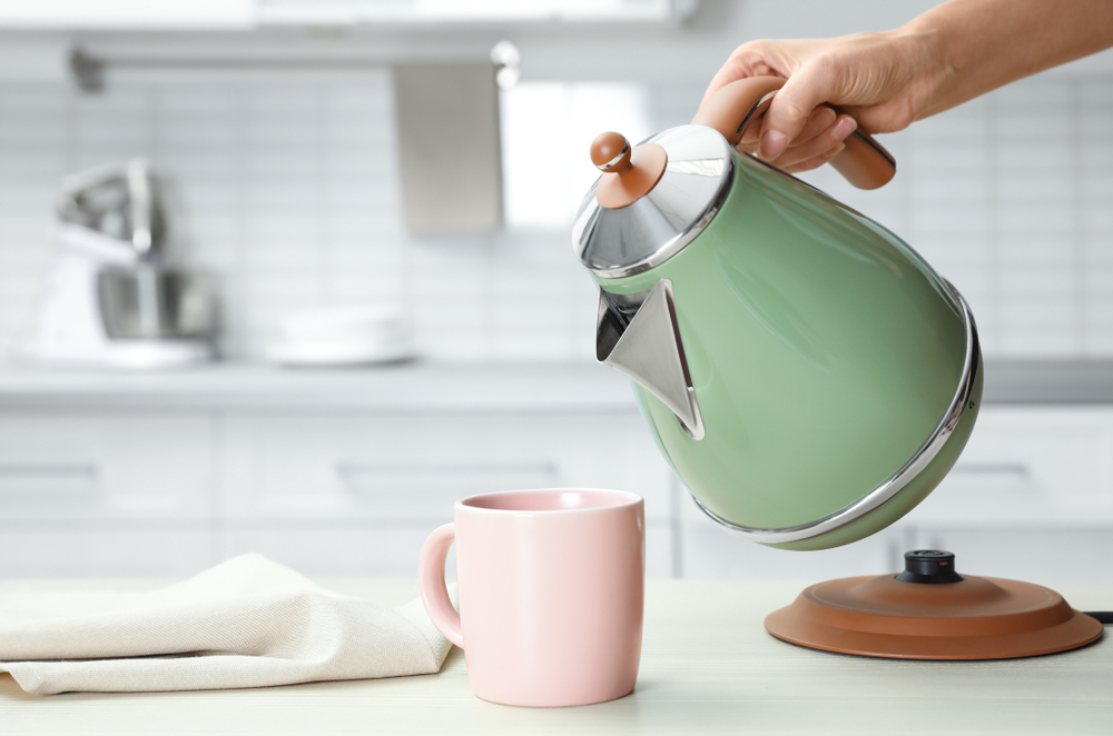 A green boiled kettle pouring water into a pink cup. 