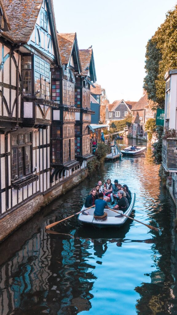 A long-shot image of the Canterbury river with a boat full of people sailing alongside an old town building.