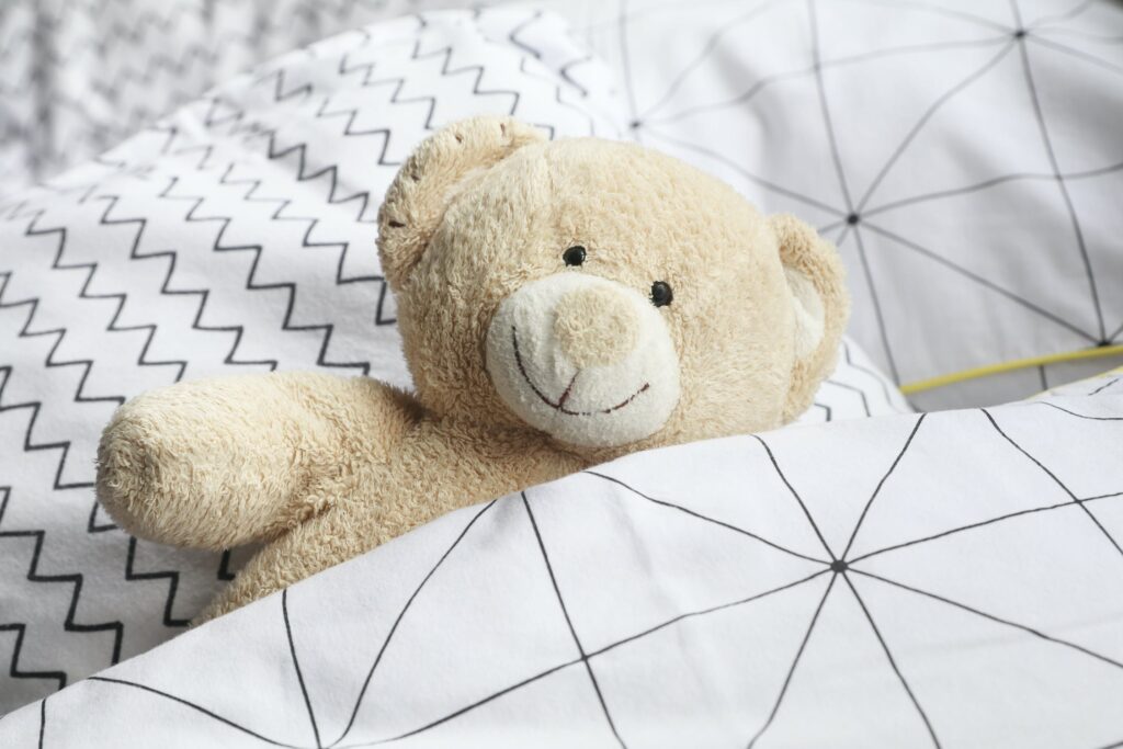 A smiling teddy bear tucked up in a white bedspread.