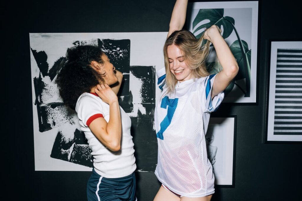 Two women dancing and laughing in a dark room.