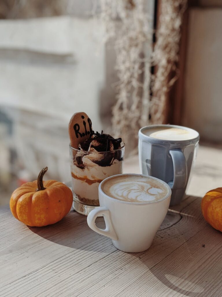 A pumpkin spice creme latte displayed on a wooden table alongside two small pumpkins.