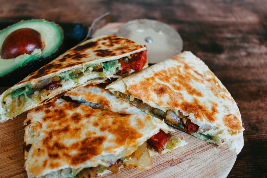 Quesadillas are served on a wooden table alongside a sliced advacado. 