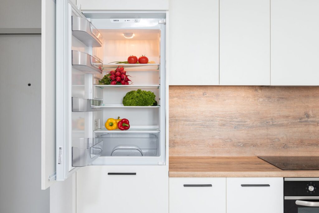 A white/wood effect kitchen with a fridge opened to reveal fruit and veg.