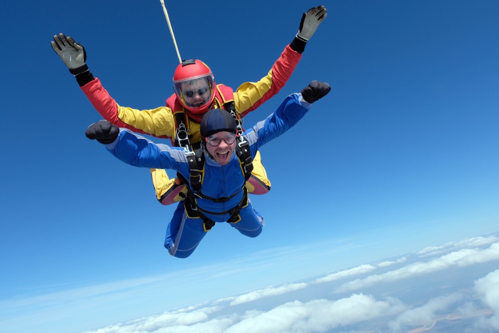 A person in a blue jump suit jumping out of a plane for breast cancer awareness month. 