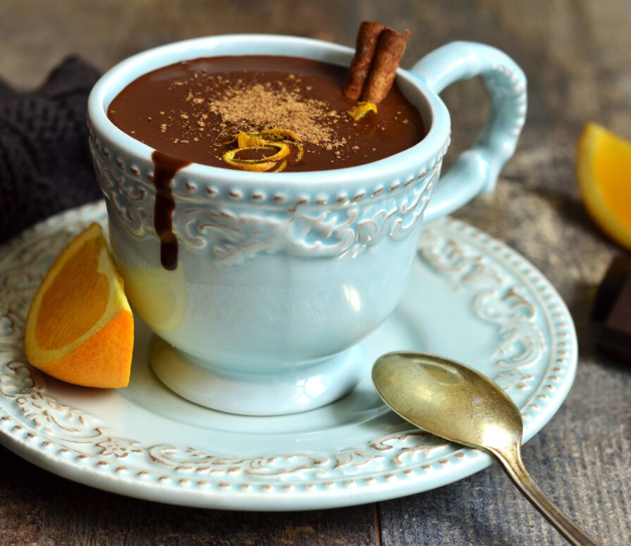 A wooden table with a cup of Cointreau orange hot chocolate with a slice of orange next to the cup. 