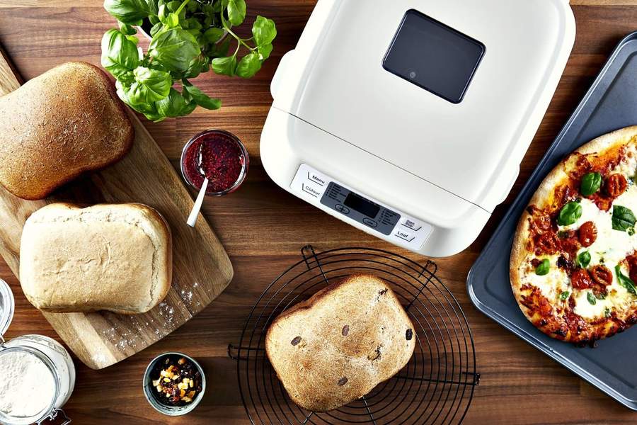 Overhead view of a bread maker, surrounded different kinds of bread and pizza.