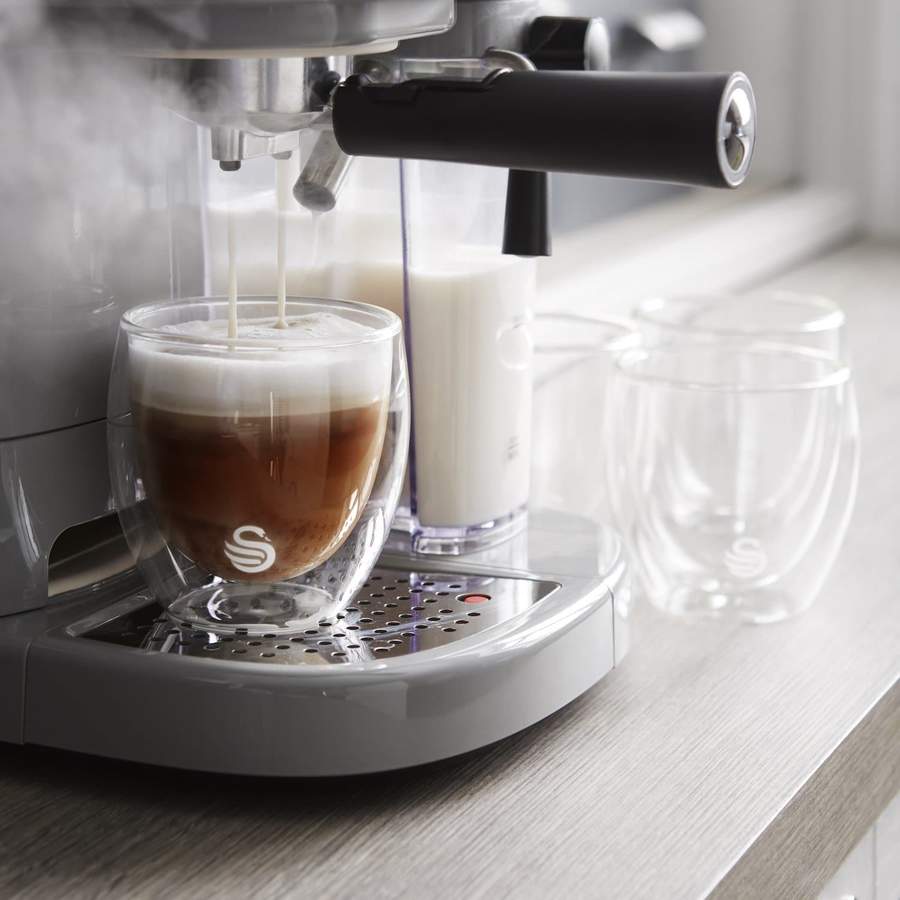 A steamy close-up of a coffee machine pouring coffee into some coffee glasses.