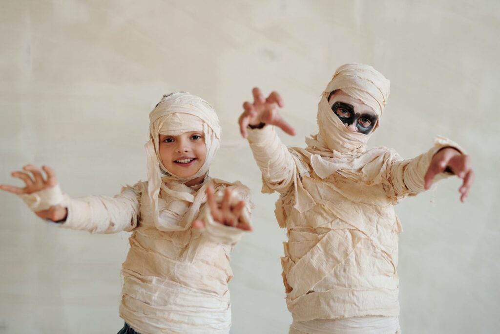Two children dressed up in mummy outfits with face paint on.