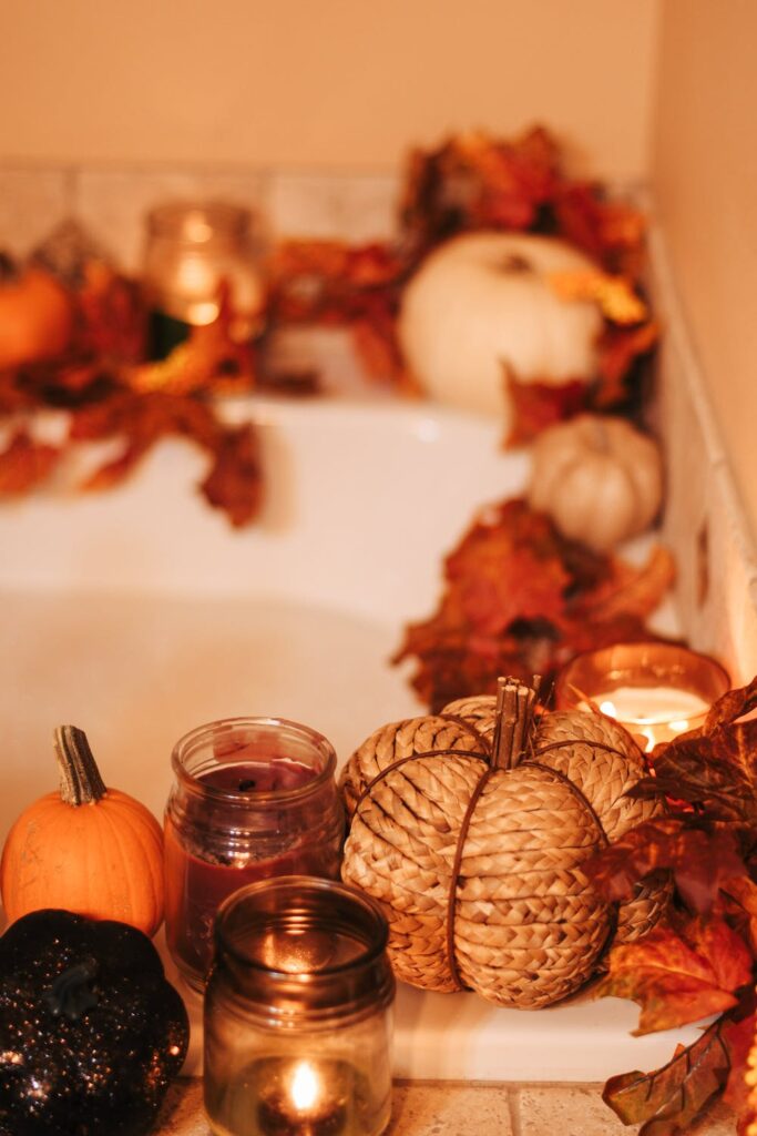 The corner shelving of a bathtub filled with small autumn-colored candles and pumpkins displayed.