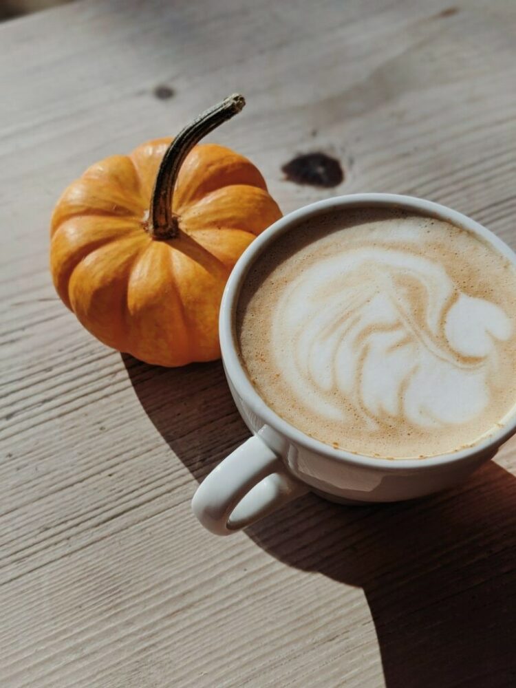 A pumpkin alongside a cup of pumpkin-spiced latte sitting on a wooden table. 