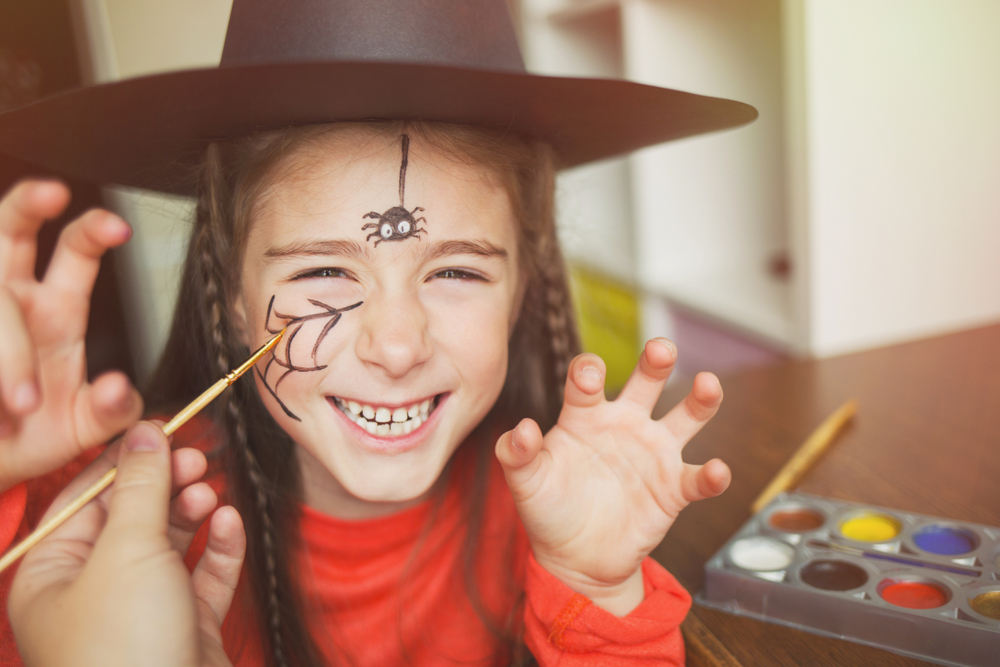 Young girl with spider face paint on, dressed up for Halloween as a witch