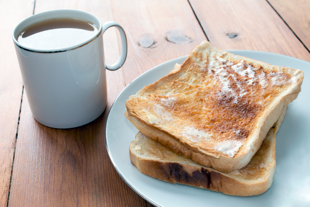A plate of white toast next to a mug of tea on a wooden table
