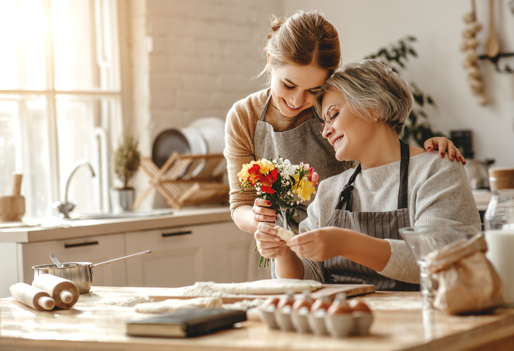 Young blonde woman and elderly mother celebrating Mother's day with flowers in their kitchen