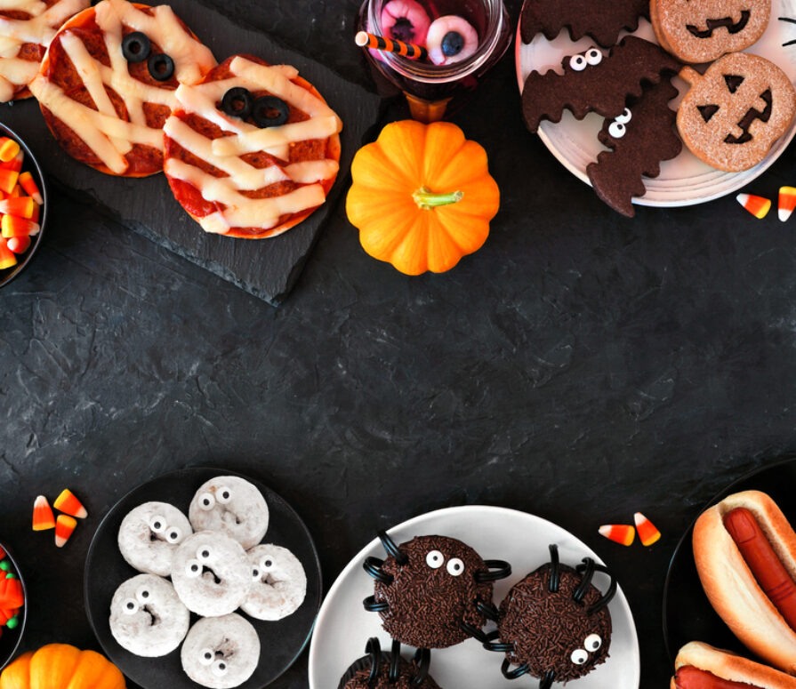A black table with mini pumpkins and small dishes of Halloween-style biscuits and desserts.