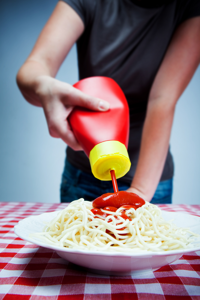 Photograph of a woman pouring ketchup onto a plate of plain spaghetti