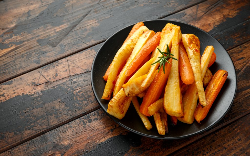 Roasted parsnips and carrots with herbs on rustic wooden tables