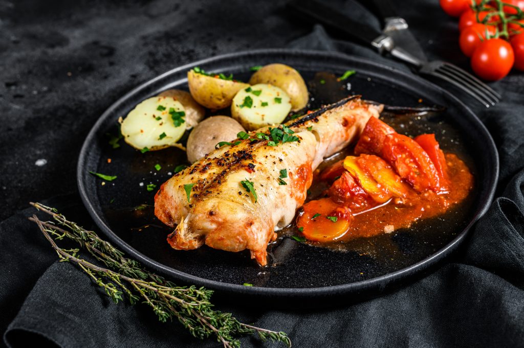 A roasted monkfish baked in tomatoes with potatoes and vegetables