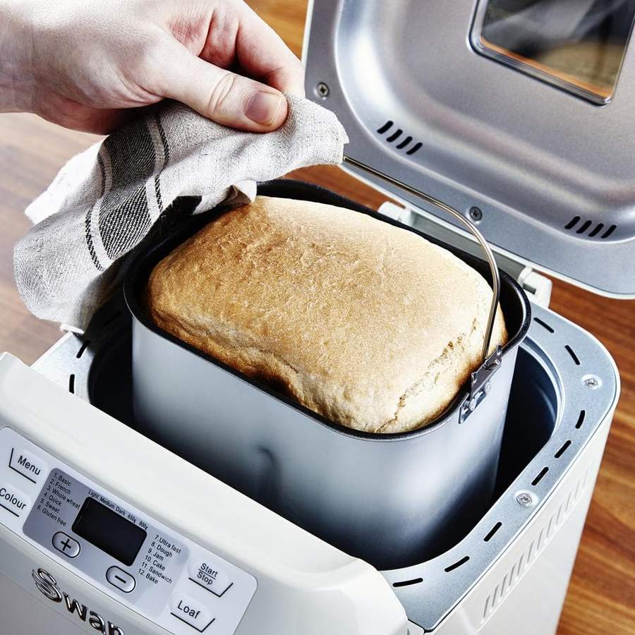 Colour image of person taking a freshly baked loaf of bread out of the Swan bread maker 
