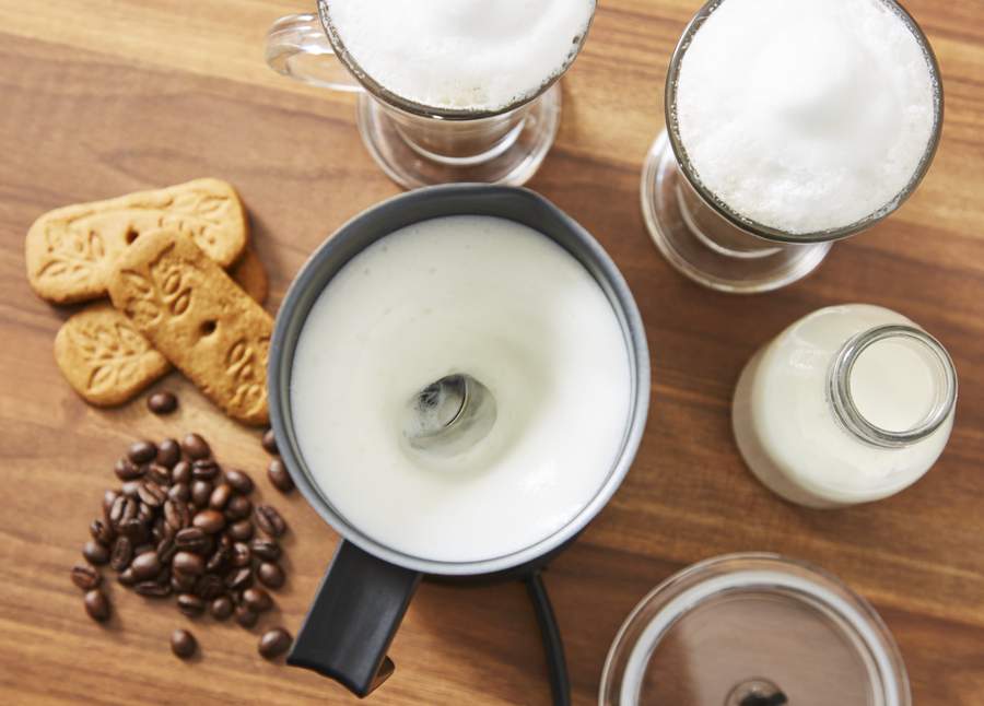 Image of the Swan Milke Frother in use, surrounded by frothy coffees, biscuits and milk 