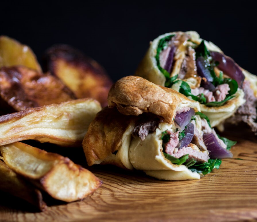 Image of a Yorkshire pudding wrap with meat and vegetables inside alongside some parsnips. 