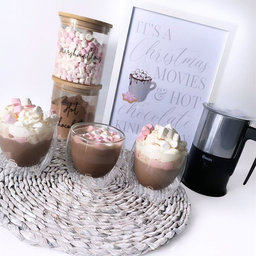 Customer product challenge photograph of the swan automatic milk frother next to a poster that reads "it's a christmas movies & hot chocolate kind of day" and three glasses of hot chocolate topped with pink and white marshmallows
