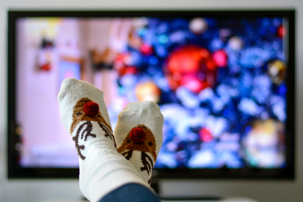 Cozy warm winter christmas socks with a reindeer. Person watching a christmas movie on the television.