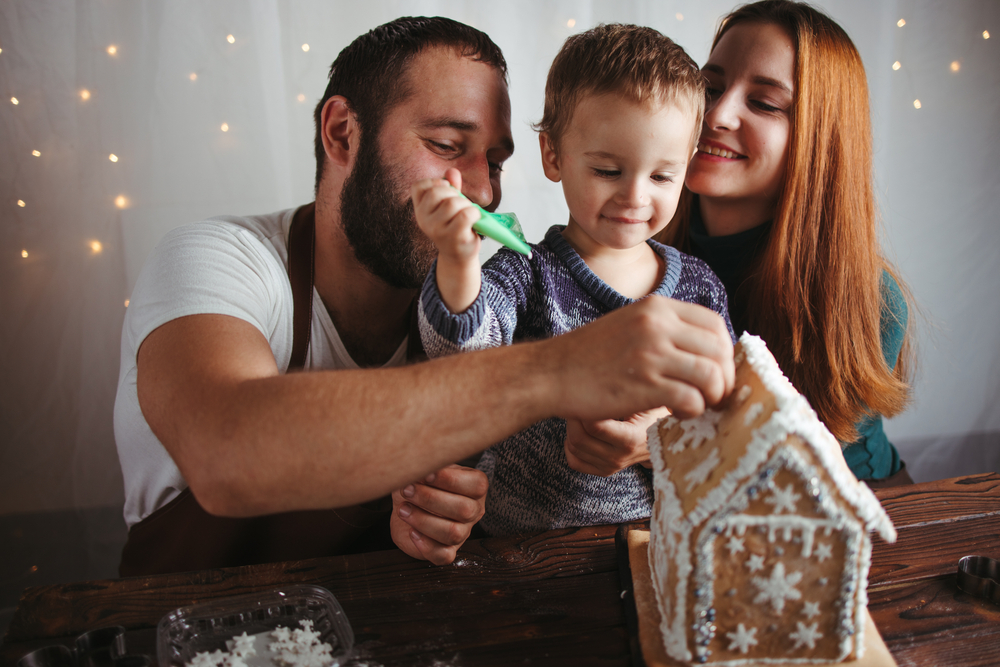 Young family spend christmas day building a gingerbread house.