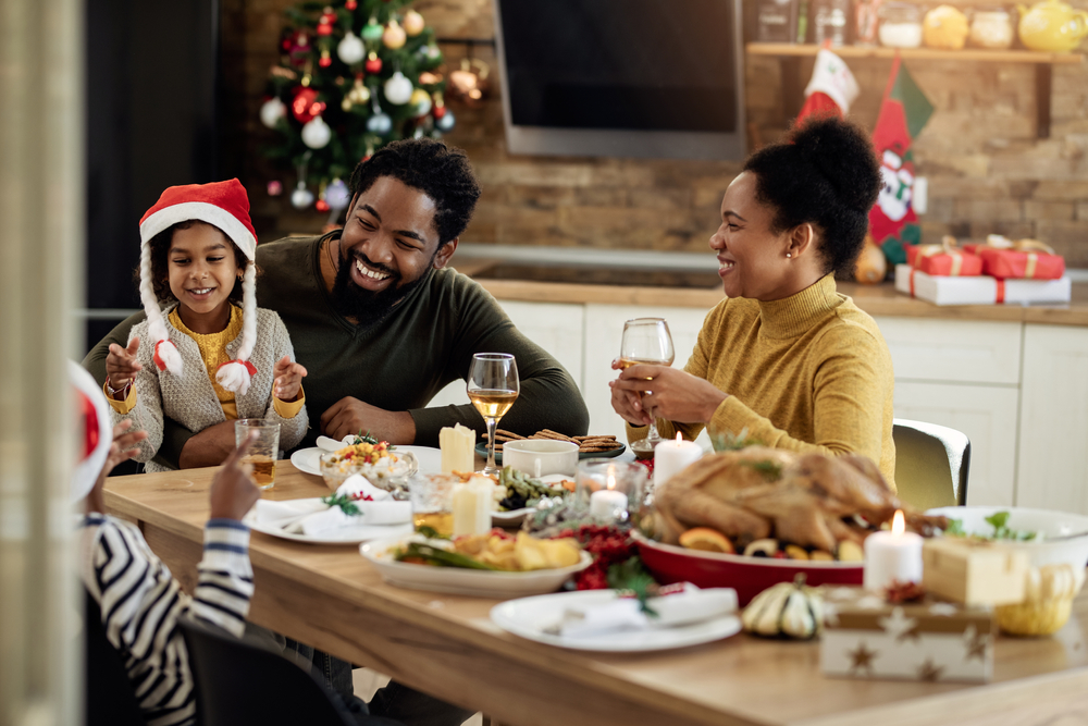 Young family spend christmas day laughing and smiling around dinner table.