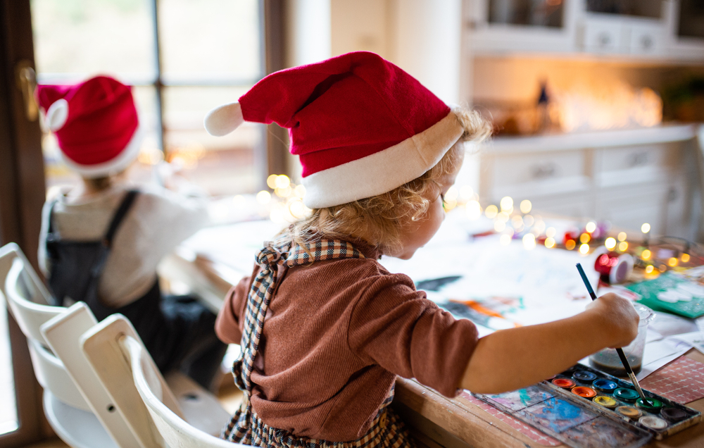 Boy and girl spend christmas day making crafts with santa hats on.