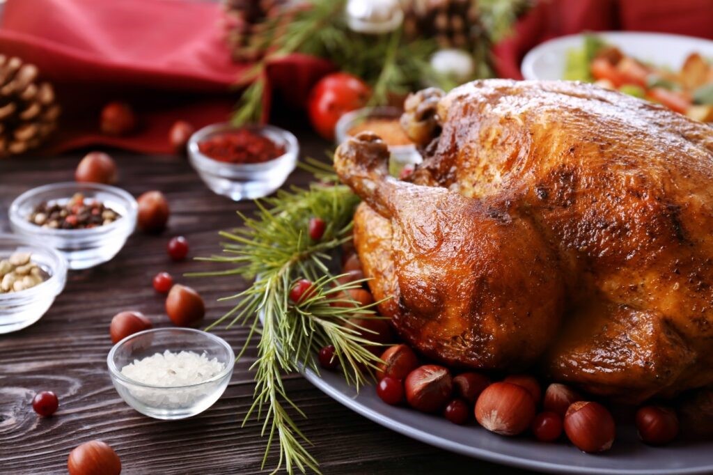 Image of a cooked Christmas turkey on a table surrounded by chestnuts, and pots of Christmas spices. 