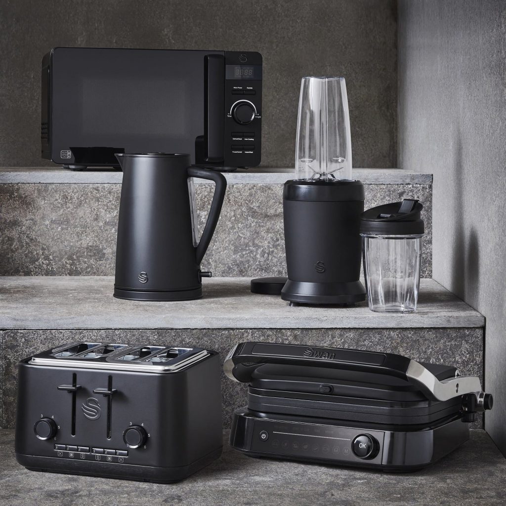 Swan Stealth matte black microwave, jug kettle, personal blender, four slice toaster and smart grill and grey granulated steps against a grey background