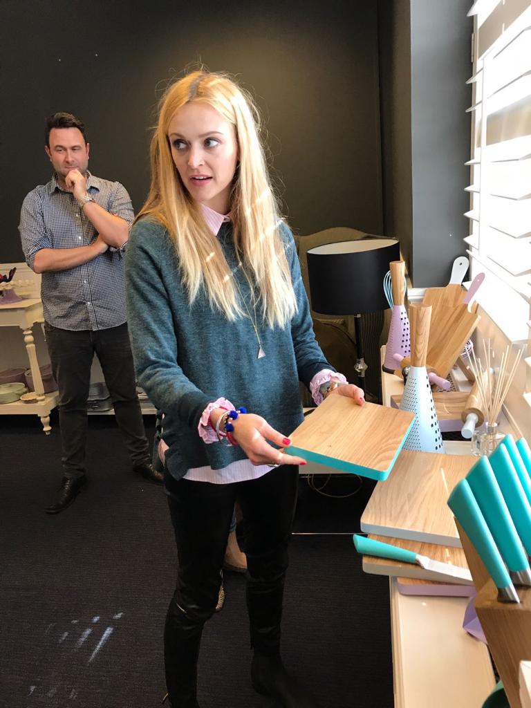 Fearne Cotton holding a chopping board next to a table holding more chopping boards and knives on the set of the Fearne by Swan Range trailer shoot