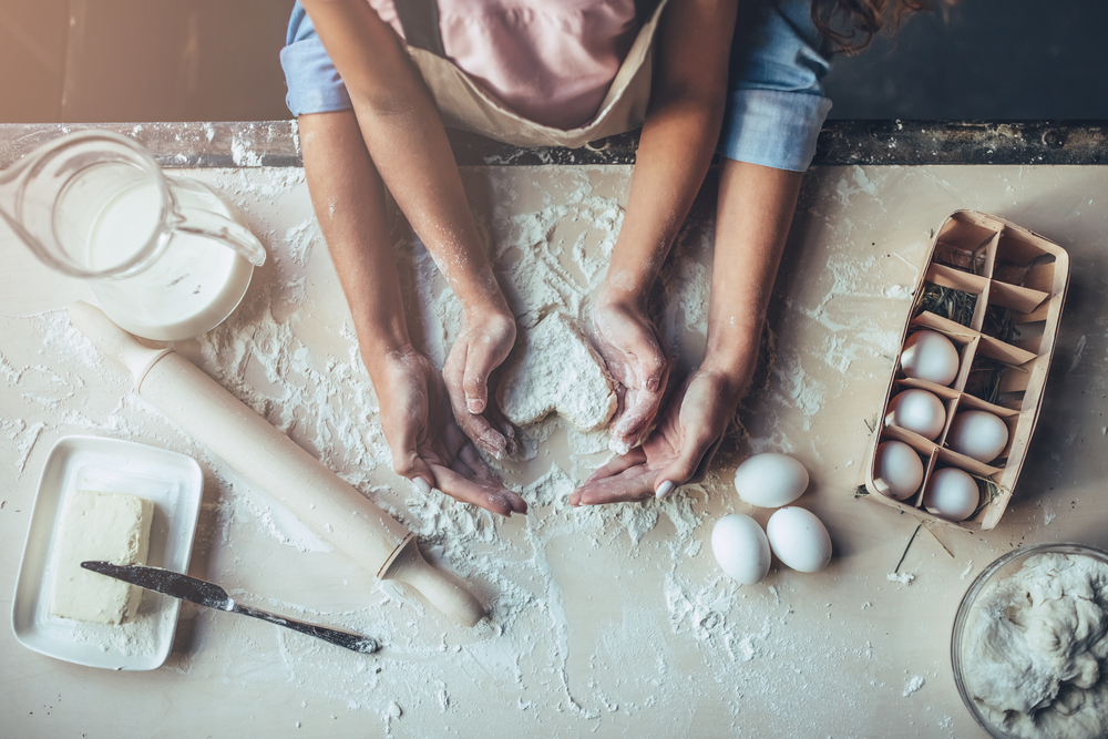 Overhead shot of a mother and daughter baking, making a heart shape out of dough and their hands