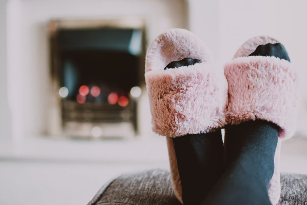 Image of a woman sat in front of a fire with her feet up in pink fluffy slippers.