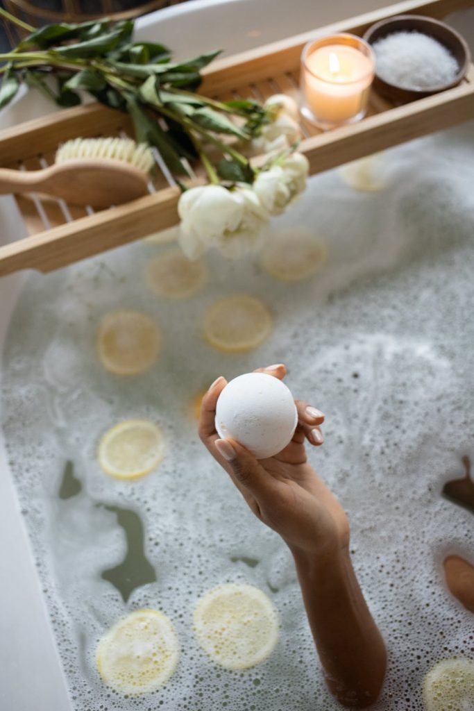 Image of a bath filled with water, a hand is come out the water holding a white bath bomb